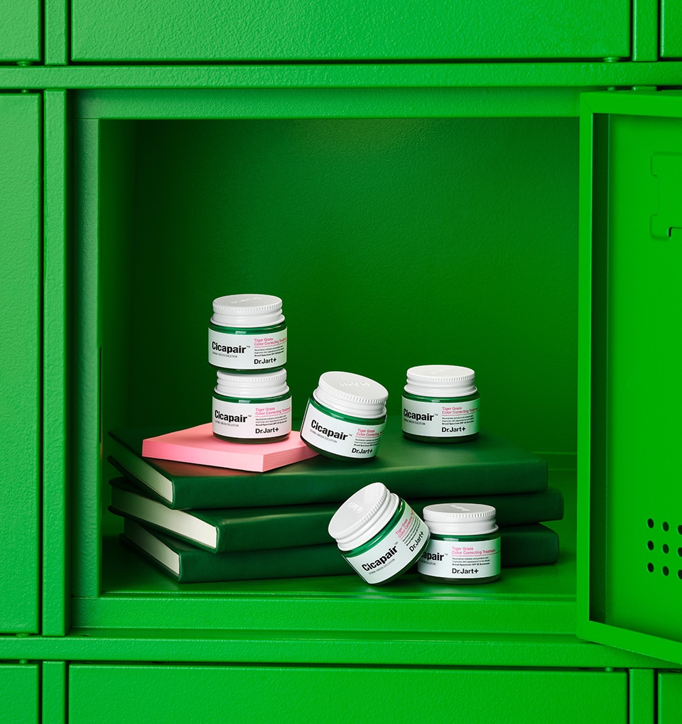 Mini jars of Dr.Jart+'s iconic Cicapair color corrector for redness are stacked on notebooks inside a bright green school locker