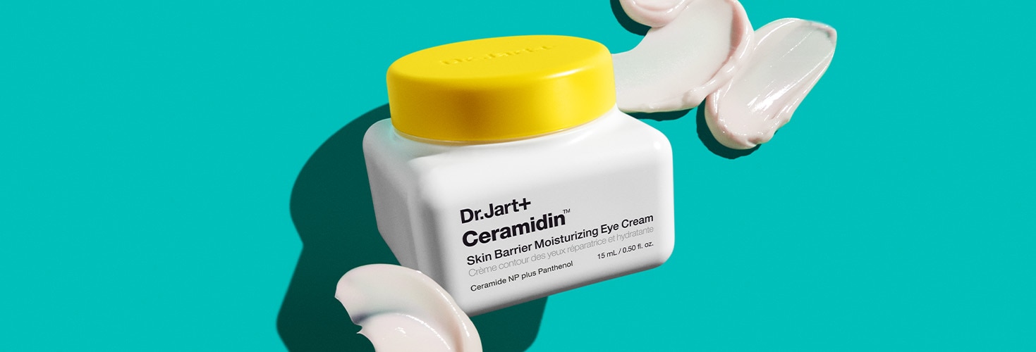 A jar of Dr.Jart+'s eye cream is displayed in front of a teal background among dollops of the eye cream's buttery texture.