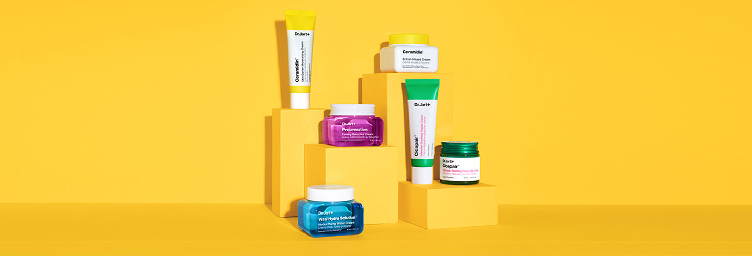 Jars and tubes of Dr.Jart+'s bestselling moisturizers stand tall in front of a bright yellow backdrop