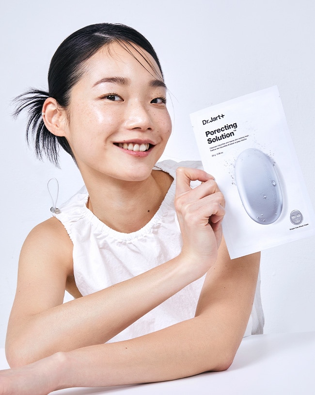 Woman holds up the packaging of a Dr.Jart+ sheet mask. 