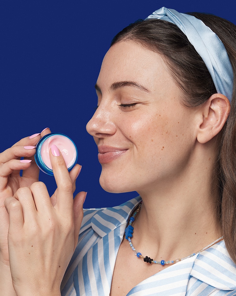 Woman applies a dollop of moisturizer cream from jar onto skin